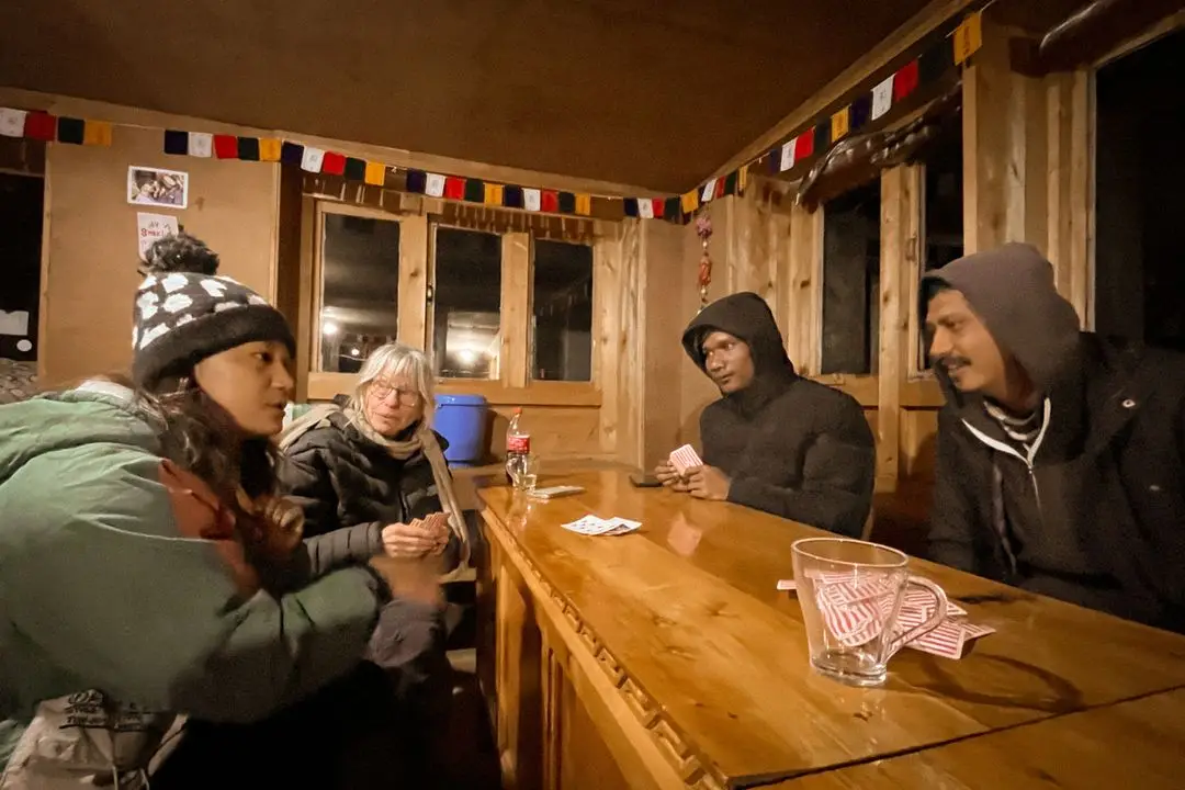 Friends play cards together at a lantern-lit table at night.