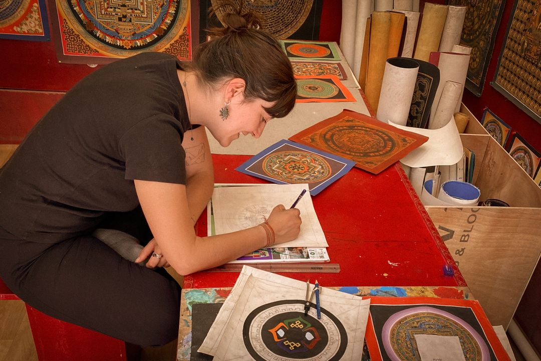 A local demonstrates traditional mandala painting at a workshop table.