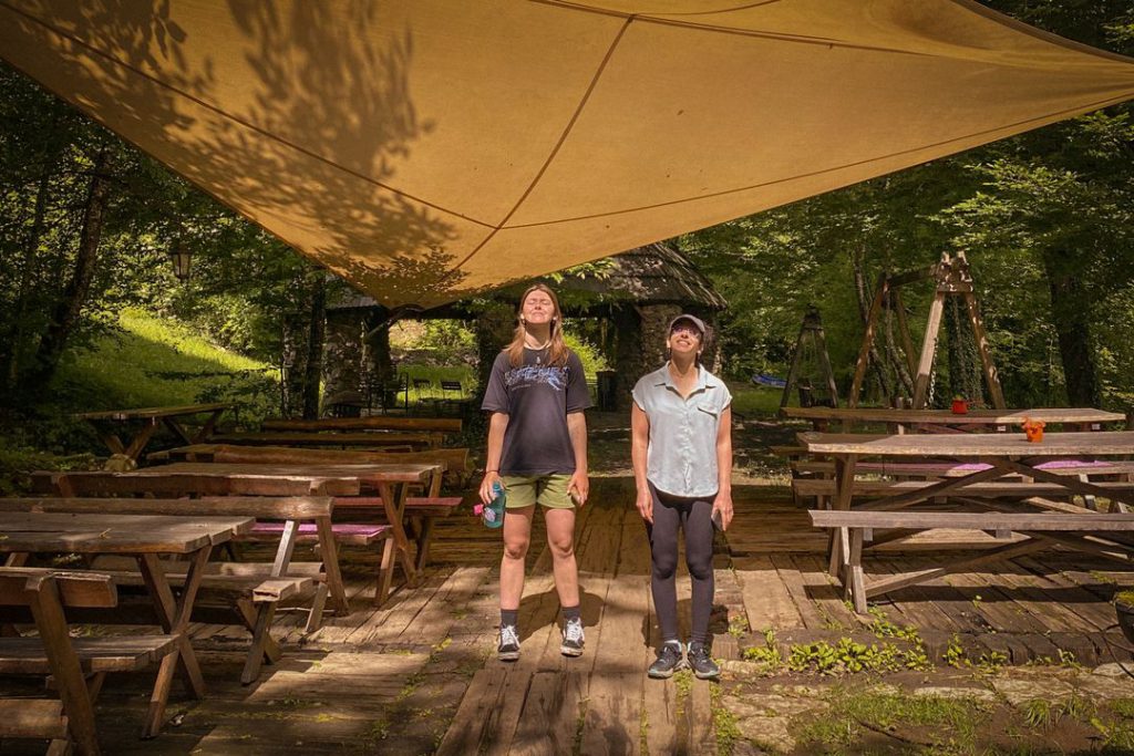 Two women stand together under a canopy shelter, surrounded by empty picnic tables.