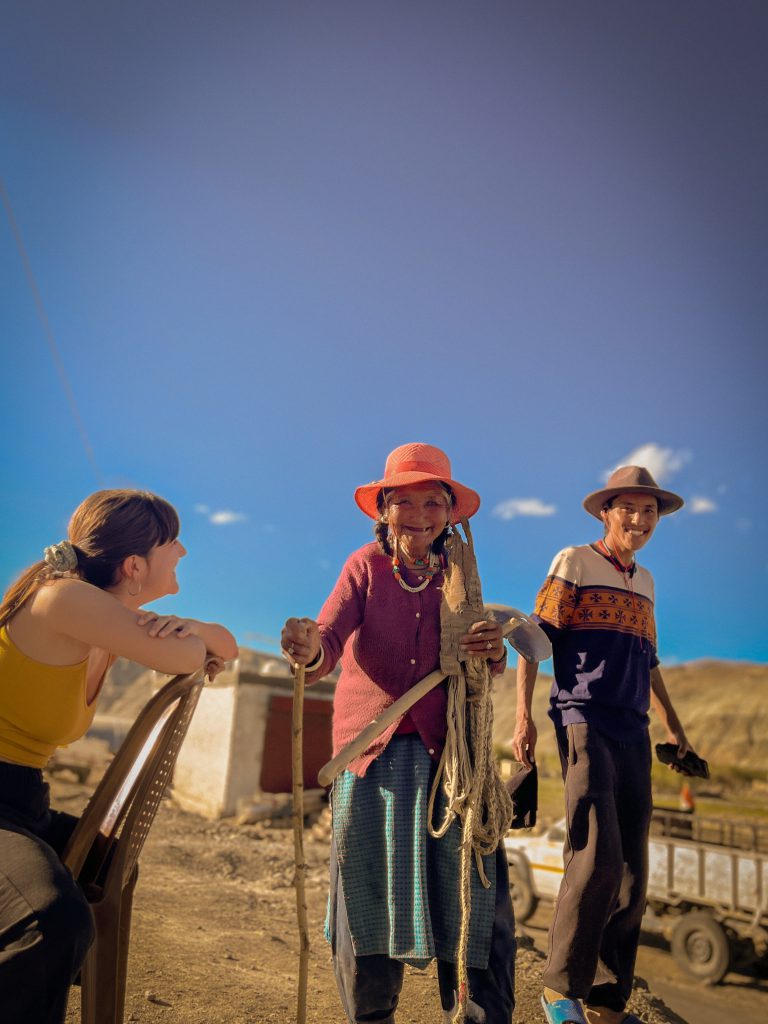 A traveler laughs with a local elder and her son during an encounter in the mountains.