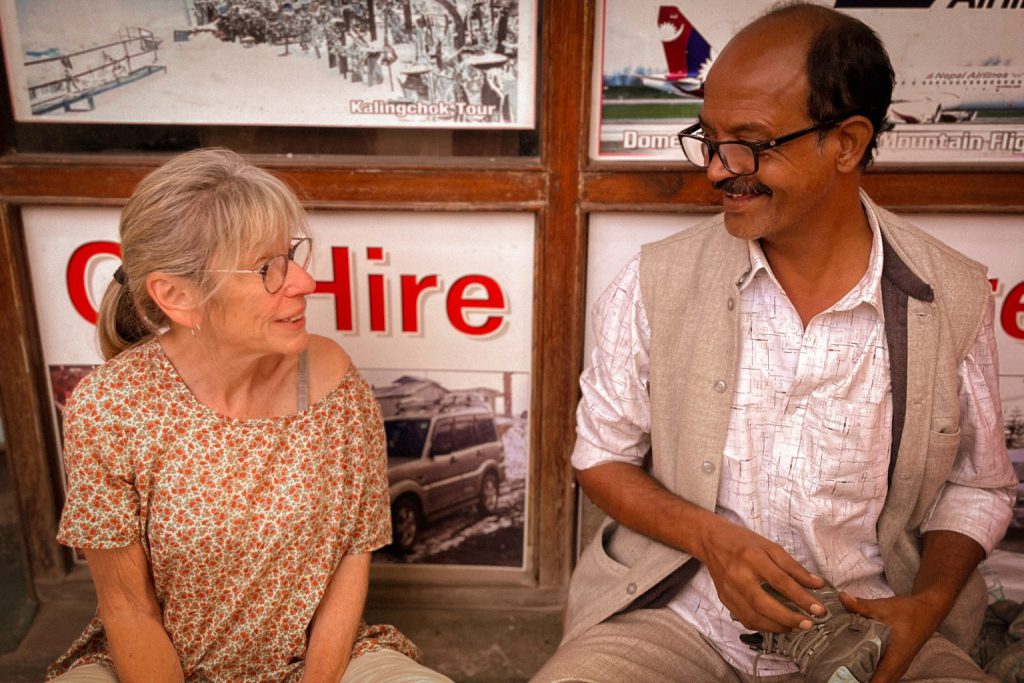 A traveler and a local chat and laugh together in front of a row of travel posters.