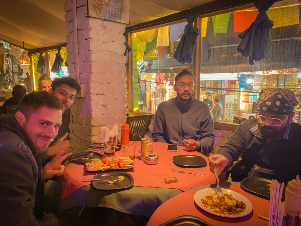 A group of friends share a meal at a lively restaurant table at night.
