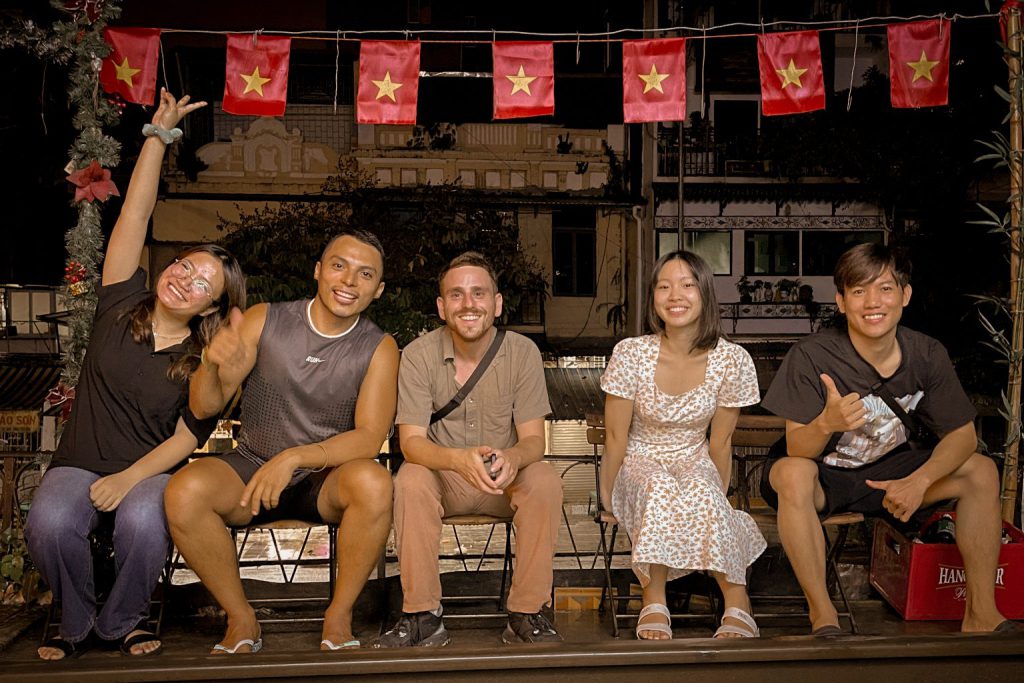 A group of friends pose together for a photo on a lively street at night.