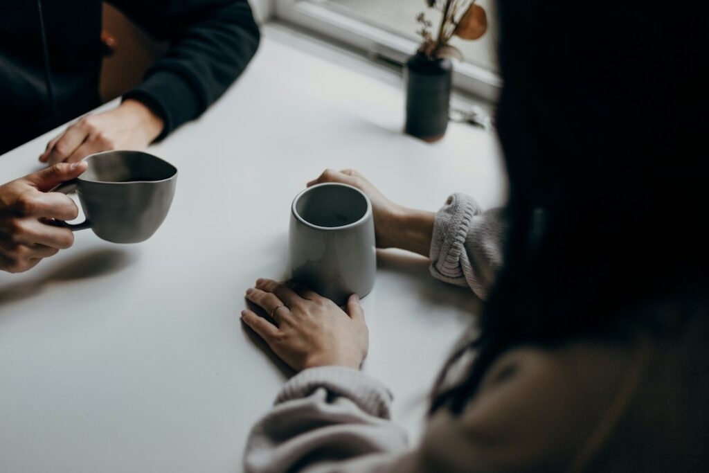 Two people holding warm mugs at a table mid conversation, a local and a traveler getting to know each other