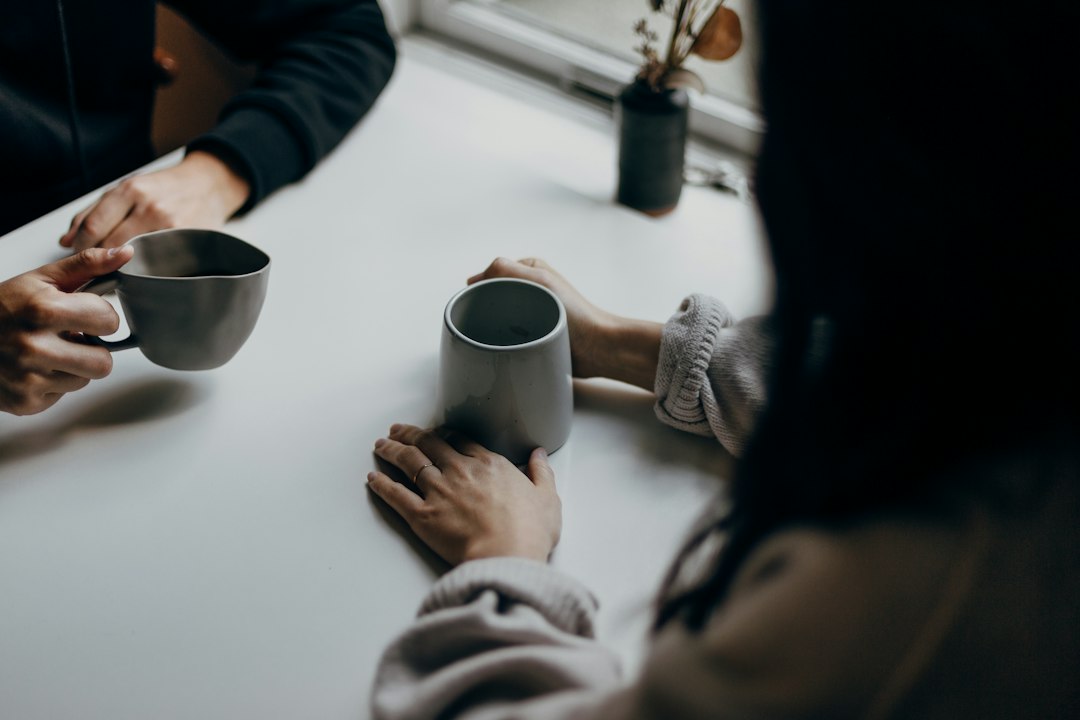 Two people holding warm mugs at a table mid conversation, a local and a traveler getting to know each other